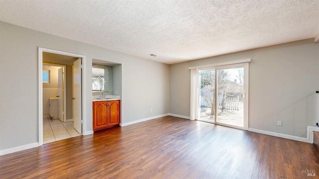 unfurnished living room with dark wood-type flooring, a sink, a textured ceiling, and baseboards