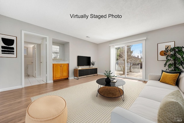 living area featuring light wood-type flooring, a textured ceiling, and baseboards