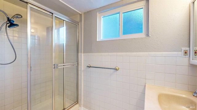 bathroom with a sink, a shower stall, tile walls, and a textured wall