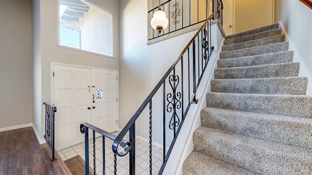 stairway with a towering ceiling, baseboards, and wood finished floors