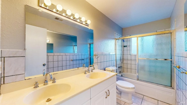 full bath with tile patterned flooring, combined bath / shower with glass door, a sink, and tile walls