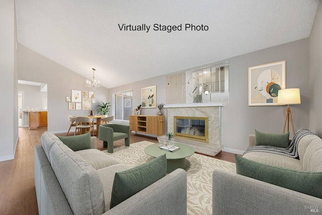 living area featuring lofted ceiling, a fireplace, wood finished floors, baseboards, and an inviting chandelier