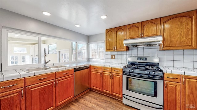 kitchen with stainless steel range with gas cooktop, brown cabinets, a sink, dishwasher, and under cabinet range hood