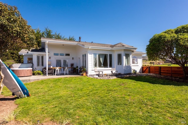 rear view of property featuring a hot tub, fence, a patio, and a yard