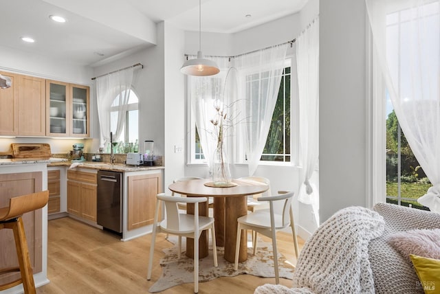 kitchen featuring light stone counters, a sink, dishwasher, light wood finished floors, and glass insert cabinets