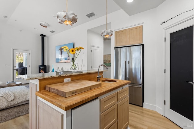 kitchen with butcher block countertops, high end refrigerator, a sink, visible vents, and light wood finished floors