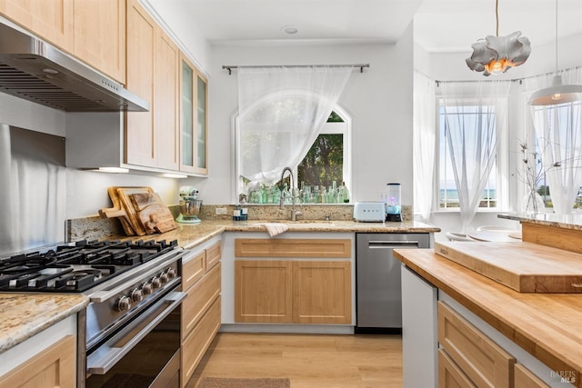 kitchen featuring under cabinet range hood, butcher block countertops, a sink, appliances with stainless steel finishes, and glass insert cabinets