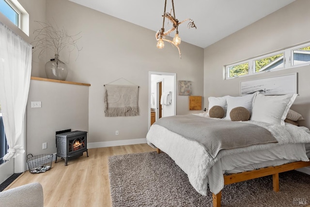 bedroom featuring multiple windows, wood finished floors, a wood stove, and baseboards