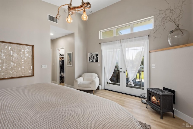 bedroom with visible vents, a towering ceiling, wood finished floors, a wood stove, and access to exterior