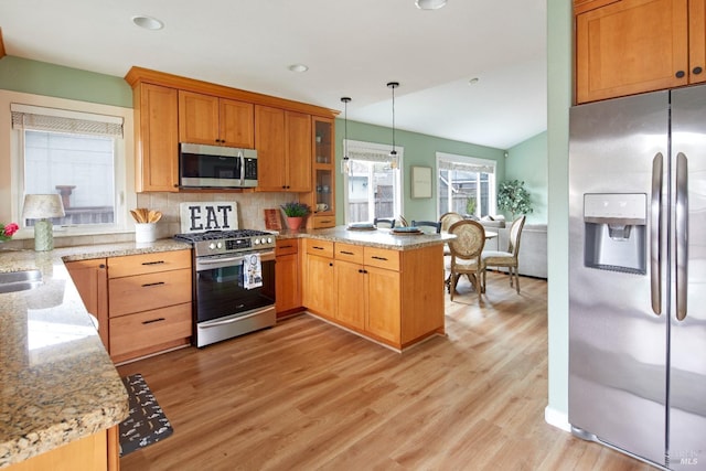 kitchen featuring light stone counters, backsplash, appliances with stainless steel finishes, a peninsula, and light wood finished floors