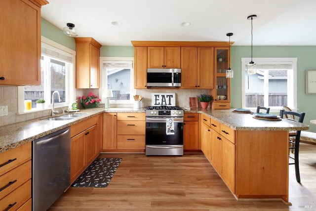 kitchen featuring light wood-style flooring, a peninsula, a kitchen breakfast bar, stainless steel appliances, and a sink