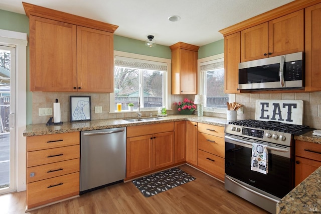 kitchen with light stone counters, appliances with stainless steel finishes, light wood-type flooring, and a sink