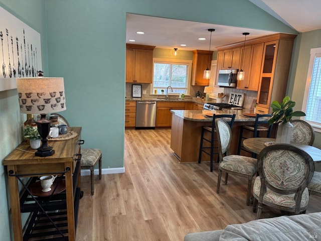 kitchen with a sink, stainless steel appliances, a peninsula, brown cabinetry, and light wood finished floors