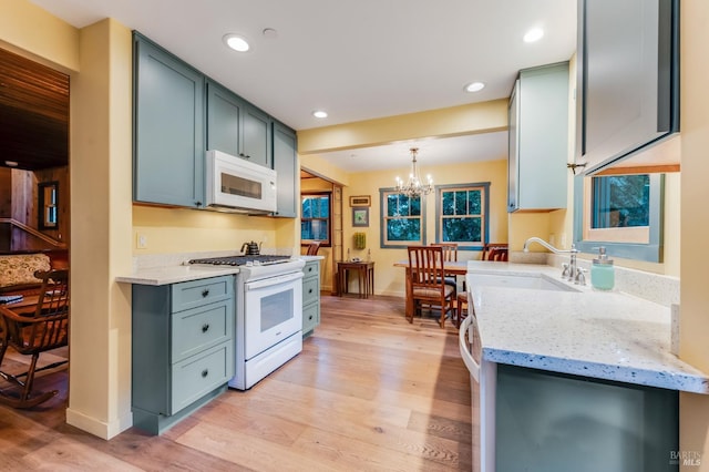 kitchen featuring white appliances, light wood-style flooring, light stone counters, a sink, and a notable chandelier