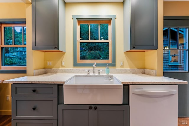 kitchen featuring gray cabinets, white dishwasher, a sink, and light stone countertops