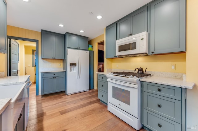 kitchen featuring light stone counters, light wood finished floors, recessed lighting, decorative backsplash, and white appliances