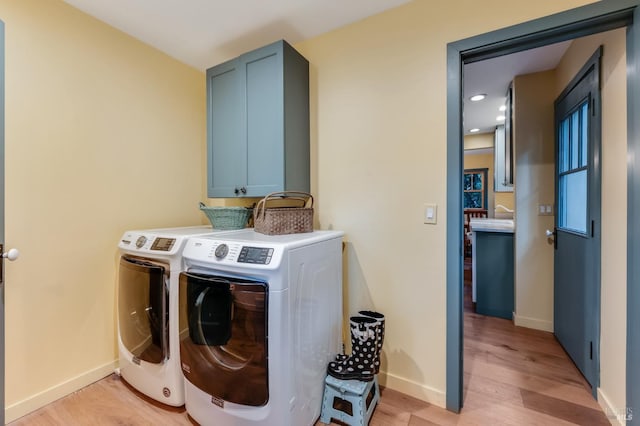 laundry room featuring light wood finished floors, washing machine and dryer, cabinet space, and baseboards