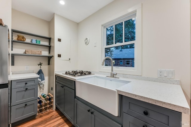 kitchen with gray cabinetry, a sink, gas stovetop, open shelves, and light wood finished floors