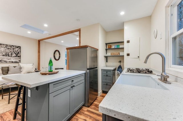 kitchen with freestanding refrigerator, gray cabinetry, light wood-type flooring, open shelves, and a sink