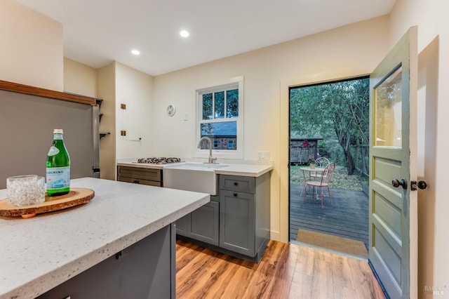 kitchen with light stone counters, gray cabinets, light wood-style floors, gas stovetop, and a sink