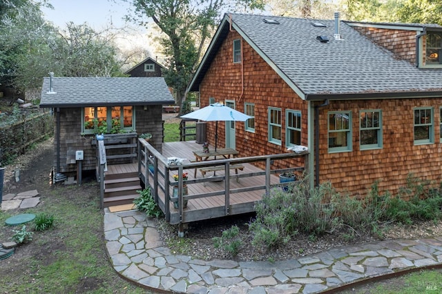 rear view of house featuring a deck, roof with shingles, and an outbuilding