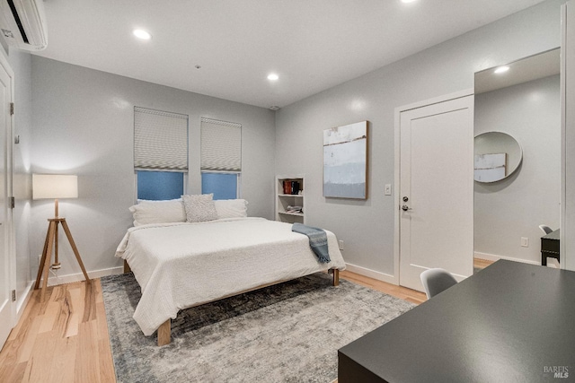 bedroom with light wood-style floors, recessed lighting, baseboards, and a wall mounted AC