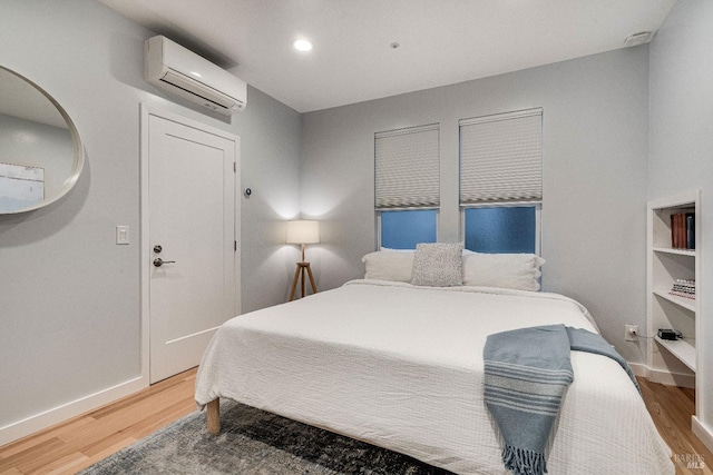 bedroom with a wall unit AC, light wood-style floors, baseboards, and recessed lighting