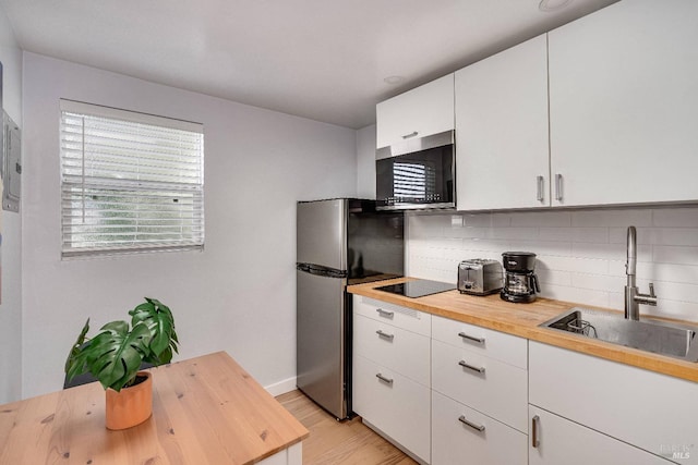 kitchen with appliances with stainless steel finishes, backsplash, butcher block countertops, and a sink