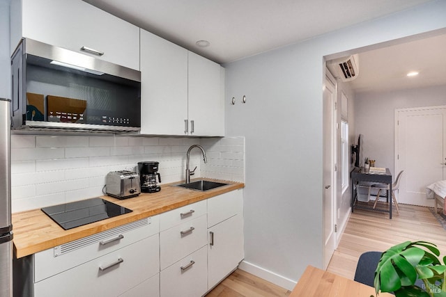 kitchen with black electric stovetop, butcher block counters, stainless steel microwave, decorative backsplash, and a sink