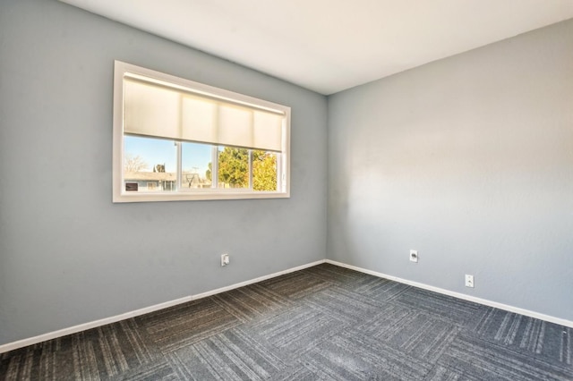 spare room featuring baseboards and dark colored carpet