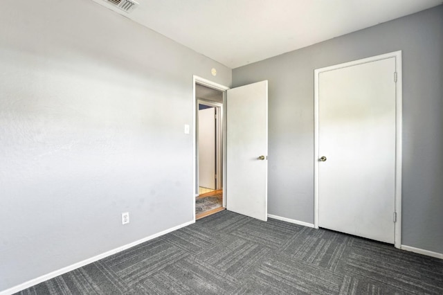 unfurnished bedroom featuring visible vents, dark carpet, and baseboards