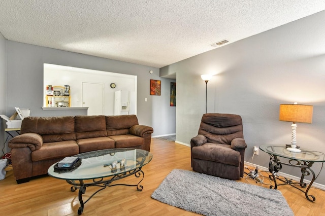 living area featuring visible vents, a textured ceiling, baseboards, and wood finished floors