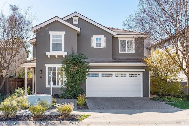 traditional home featuring a garage, fence, decorative driveway, and stucco siding