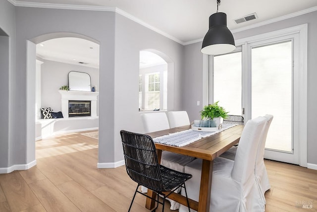 dining area featuring visible vents, baseboards, light wood-type flooring, a glass covered fireplace, and crown molding