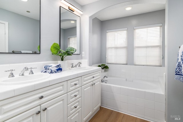 full bath with double vanity, a garden tub, a sink, and wood finished floors