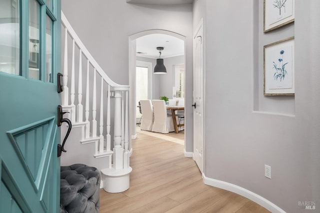 foyer entrance featuring stairway, arched walkways, light wood-style flooring, and baseboards