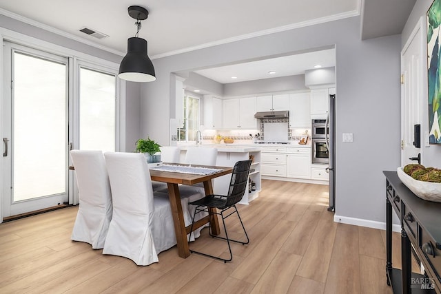 dining space with baseboards, light wood-style flooring, visible vents, and crown molding