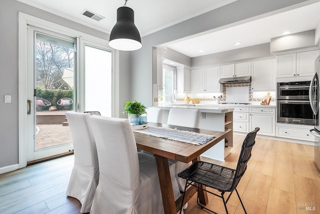 dining space with ornamental molding, light wood finished floors, plenty of natural light, and visible vents