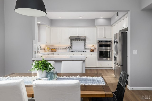 kitchen with tile countertops, stainless steel appliances, white cabinetry, a sink, and under cabinet range hood