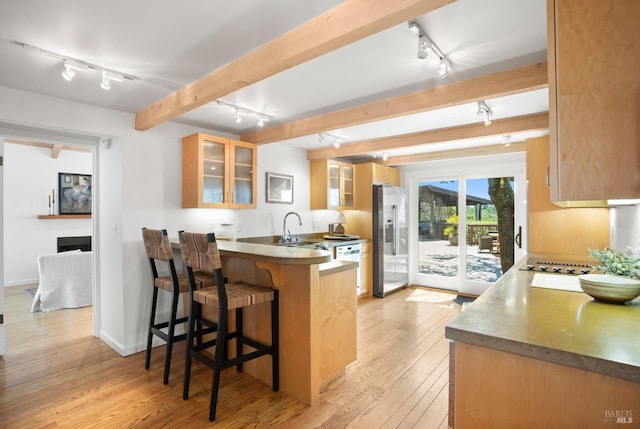 kitchen with light wood finished floors, a breakfast bar area, a peninsula, stainless steel appliances, and beam ceiling