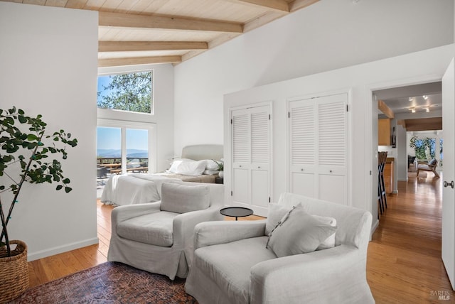 bedroom featuring high vaulted ceiling, beamed ceiling, two closets, and wood finished floors