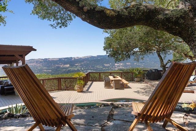 wooden deck featuring an in ground hot tub, outdoor dining space, and a mountain view