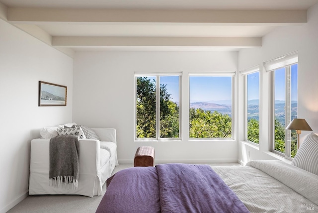 bedroom featuring multiple windows, beamed ceiling, light carpet, and a mountain view