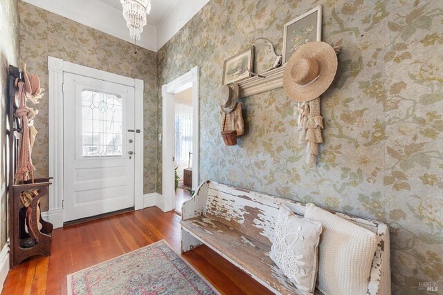 entrance foyer with wallpapered walls, a notable chandelier, wood finished floors, and baseboards