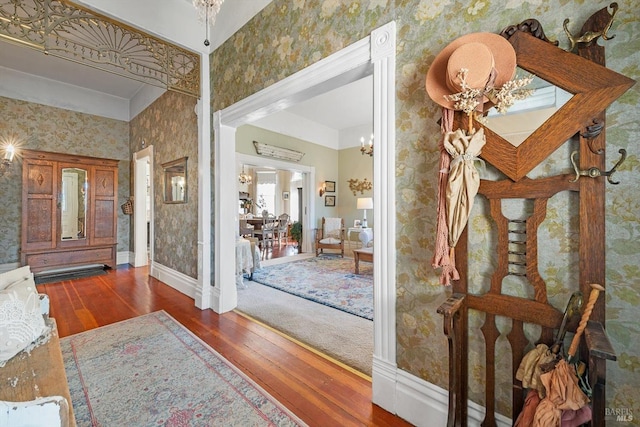 foyer with baseboards, wallpapered walls, an inviting chandelier, and wood finished floors