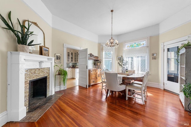 dining room with an inviting chandelier, hardwood / wood-style flooring, a fireplace, and baseboards