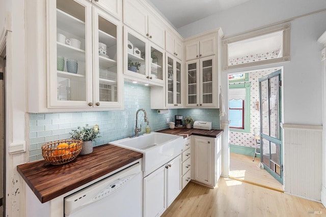 kitchen with light wood finished floors, glass insert cabinets, white dishwasher, wood counters, and a sink