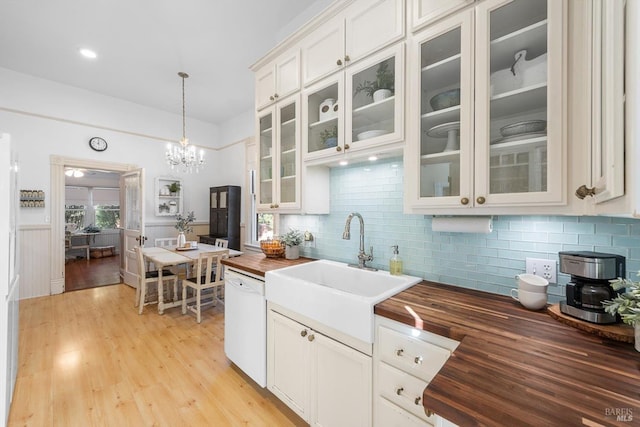 kitchen with a sink, light wood-style floors, white dishwasher, wooden counters, and hanging light fixtures