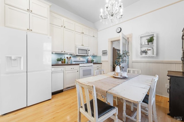 kitchen featuring white appliances, light wood finished floors, an inviting chandelier, white cabinets, and wainscoting