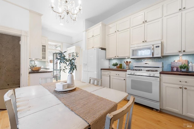 kitchen with light wood finished floors, backsplash, an inviting chandelier, white cabinets, and white appliances